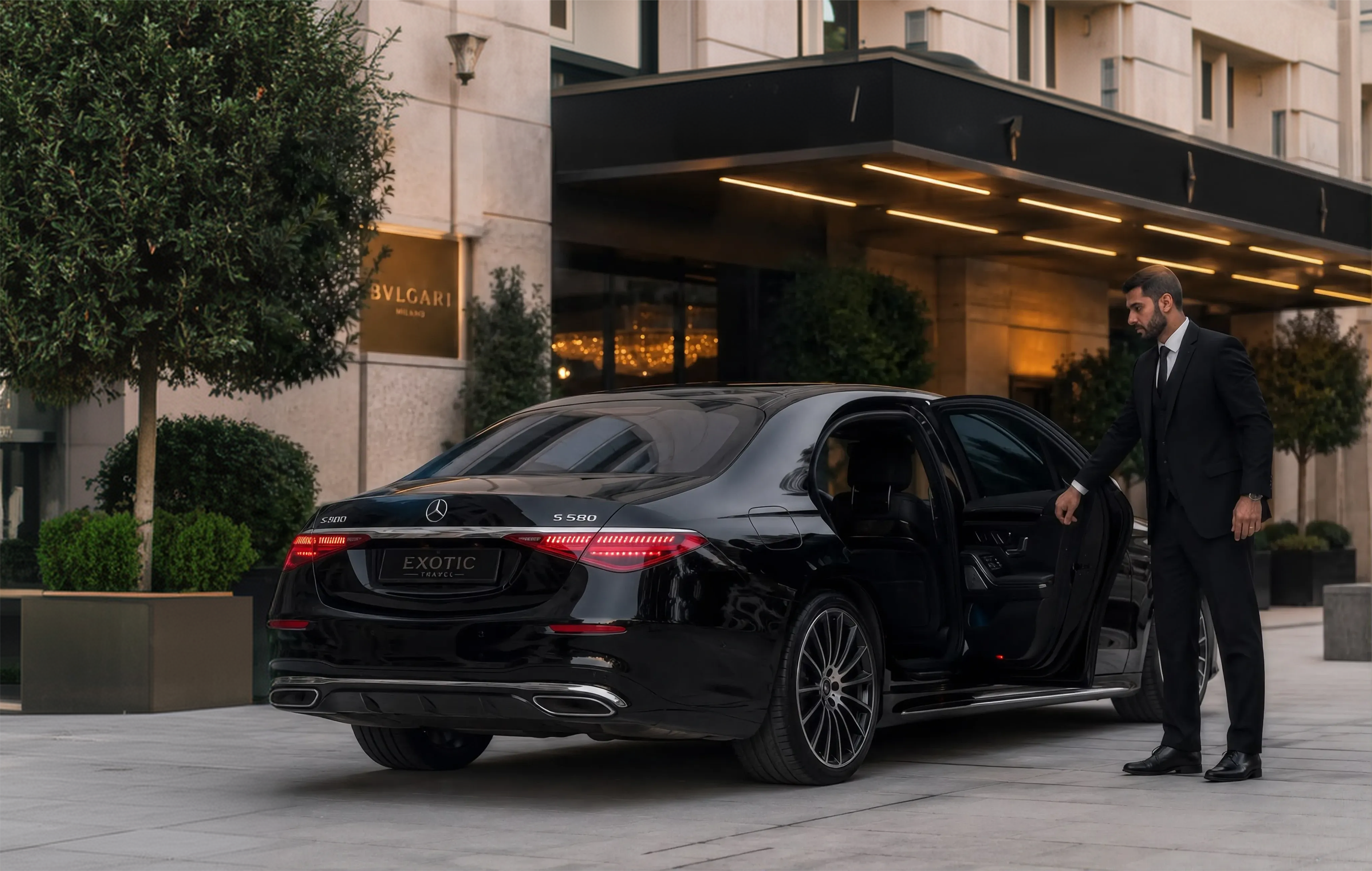 A chauffeur opening the rear door of a black Mercedes S-Class at a luxury hotel entrance